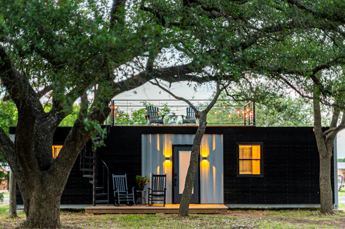 Small dark-sided backyard cottage under an oak tree, lit at dusk